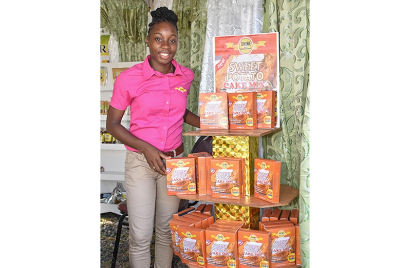 Guyana School of Agriculture graduate, Ms. Kelshine Griffith, who now owns Shine Agri Manufacturing, stands beside a display of her pilot agro-processing product, boxed Sweet Potato Cake Mix. (Guyana Chronicle photo)