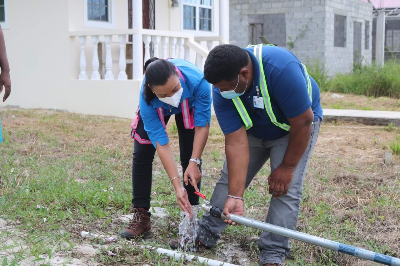 Water flows from a newly installed individual service connection. In the photo are: Minister within the Ministry of Housing and Water, Susan Rodrigues & GWI's East Bank Demerara Manager, Mr. Nishaul Samaroo