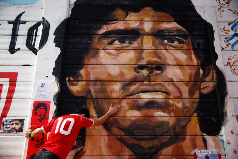 A boy touches a mural of Diego Maradona outside the stadium of Argentinos Juniors soccer club [Marcos Brindicci/AP Photo]