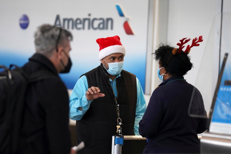 A passenger approaches two airline workers in Christmas-themed headwear at Ronald Reagan Washington National Airport, in Arlington, Virginia, US, December 22, 2020 [Kevin Lamarque/ Reuters]