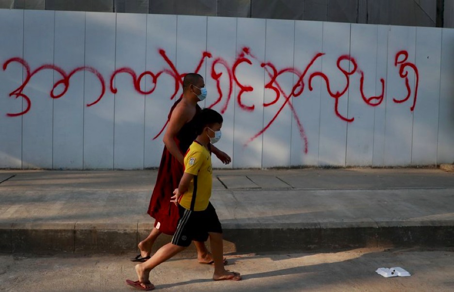 Pedestrians pass by a graffiti reading as "don't want dictatorship" in Yangon, Myanmar, Tuesday, Feb. 4, 2021. Myanmar's new military government has blocked access to Facebook as resistance to Monday's coup surged amid calls for civil disobedience to protest the ousting of the elected civilian government and its leader Aung San Suu Kyi. (AP Photo)