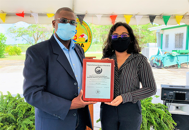 (L-R) Dr. Dane Hartley, Head of the Veterinary Services Laboratory, and Quality Manager Cherie Rampertab pose with the plaque presented to the Laboratory by the GNBS