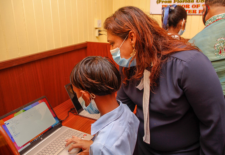 Minister Manickchand assisting a student of the No. 59 Primary School with using one of the laptops in the new Learning Centre at the school