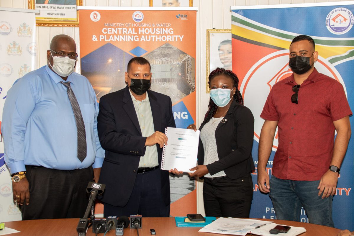 Minister of Housing & Water, Collin Croal hands over the contract for the construction of core homes to a representative from Tristar Industries Inc., in the presence of Permanent Secretary, Mr. Andre Ally [right] and CEO of CH&PA, Mr. Sherwyn Greaves [left]