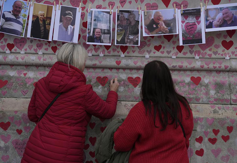 FILE - Family members write a message to two sisters who died of COVID on the National Covid Memorial wall in London, Tuesday, March 29, 2022. Latest figures from Britain's statistics agency show the prevalence of COVID-19 in the U.K. has reached record levels, with about 1 in 13 people estimated to be infected with the virus in the past week. Some 4.9 million people were estimated to have the virus in the week ending March 26, up from 4.3 million recorded in the previous week, the Office for National Statistics said Friday, April 1, 2022. (AP Photo/Alastair Grant, File)
