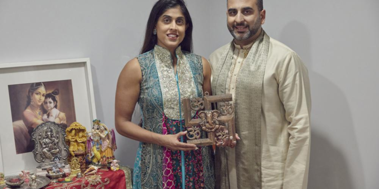 Sheetal Deo and her husband, Sanmeet Deo, hold a Hindu swastika symbol in their home in Syosset, N.Y., on Sunday, Nov. 13, 2022. Hindus, Buddhists and Native Americans are trying to rehabilitate the swastika, a symbol of peace and prosperity, and to restore it to a place of sanctity in their faiths. (AP Photo/Andres Kudacki)
