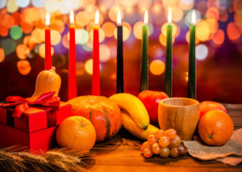 Kwanzaa holiday concept with decorate seven candles red, black and green, gift box, pumpkin, bowl and fruit on light blur bokeh background
