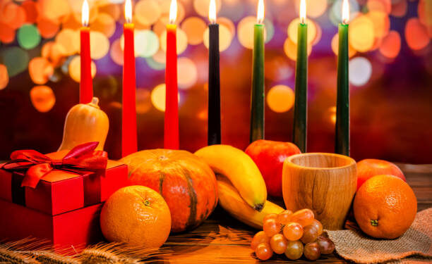 Kwanzaa holiday concept with decorate seven candles red, black and green, gift box, pumpkin, bowl and fruit on light blur bokeh background