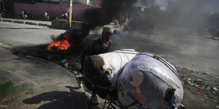 A street vendor walks past a burning barricade that was set up by members of the police as they protest bad police governance, in Port-au-Prince, Haiti, Thursday, January 26, 2023. (AP Photo/Odelyn Joseph)