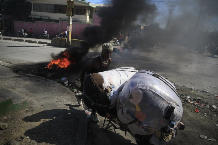 A street vendor walks past a burning barricade that was set up by members of the police as they protest bad police governance, in Port-au-Prince, Haiti, Thursday, January 26, 2023. (AP Photo/Odelyn Joseph)