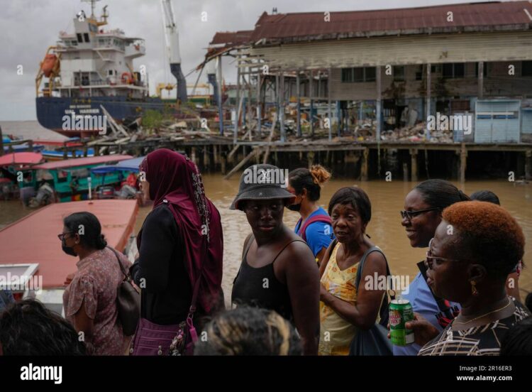People wait at the Stabroek Market to ferry across the Demerara River, near a container ship in Georgetown, Guyana, on April 12, 2023. Photo: Alamy