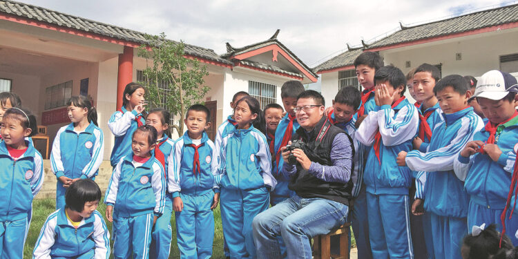 Bian Huawei prepares to take photos of students at Runan Primary School in Yulong Naxi autonomous county, Yunnan province, during a visit. CHINA DAILY
