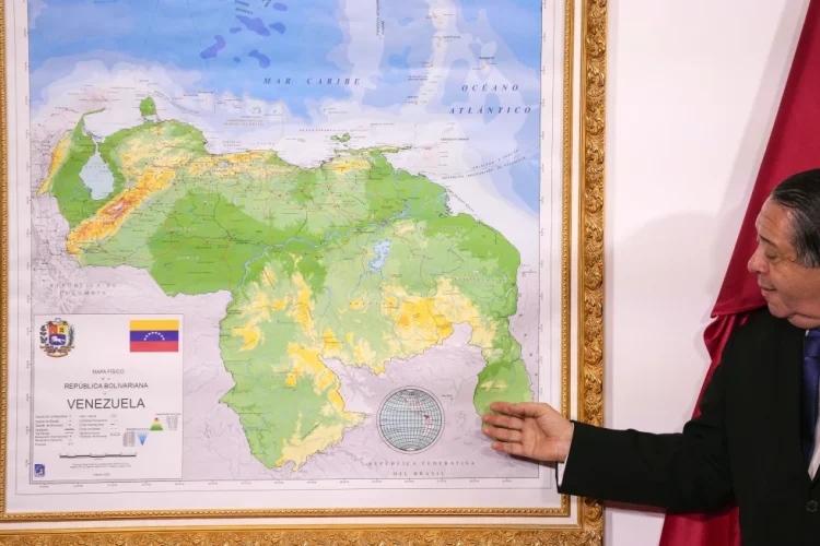 FILE - Chairman of the Special Commission for the Defense of Guyana Essequibo Hermann Escarra, stands next to Venezuela’s new map that includes the Essequibo territory, a swath of land that is administered and controlled by Guyana but claimed by Venezuela, during an unveiling ceremony in Caracas, Venezuela, Dec. 8, 2023. Venezuelan military officials said Saturday, Dec. 30, 2023, that they will continue to deploy nearly 6,000 troops until a British military vessel sent to neighboring Guyana leaves the waters off the coast of the two South American nations. (AP Photo/Matias Delacroix, File)