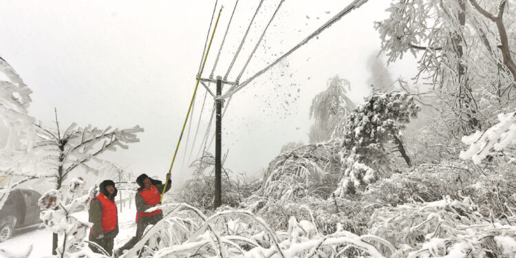 Workers remove ice and snow on power lines in Zhanjiapo village, Xiangyang, Hubei province, on Feb 6, 2024. [Photo by Yang Tao/For China Daily]