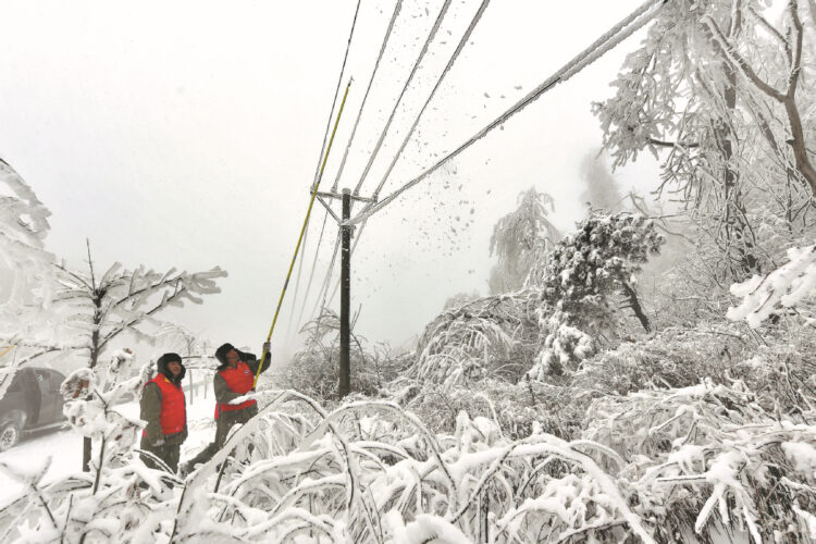 Workers remove ice and snow on power lines in Zhanjiapo village, Xiangyang, Hubei province, on Feb 6, 2024. [Photo by Yang Tao/For China Daily]