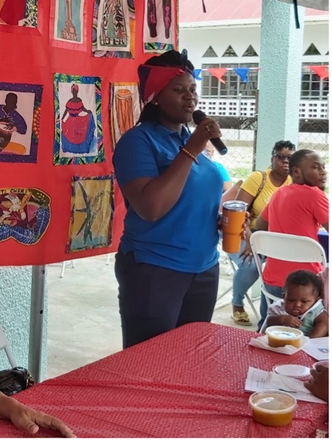 Norvelline Norvin, Secretary of AHNIG standing in front of the “Haiti/Ayiti–Our heart” Quilt
