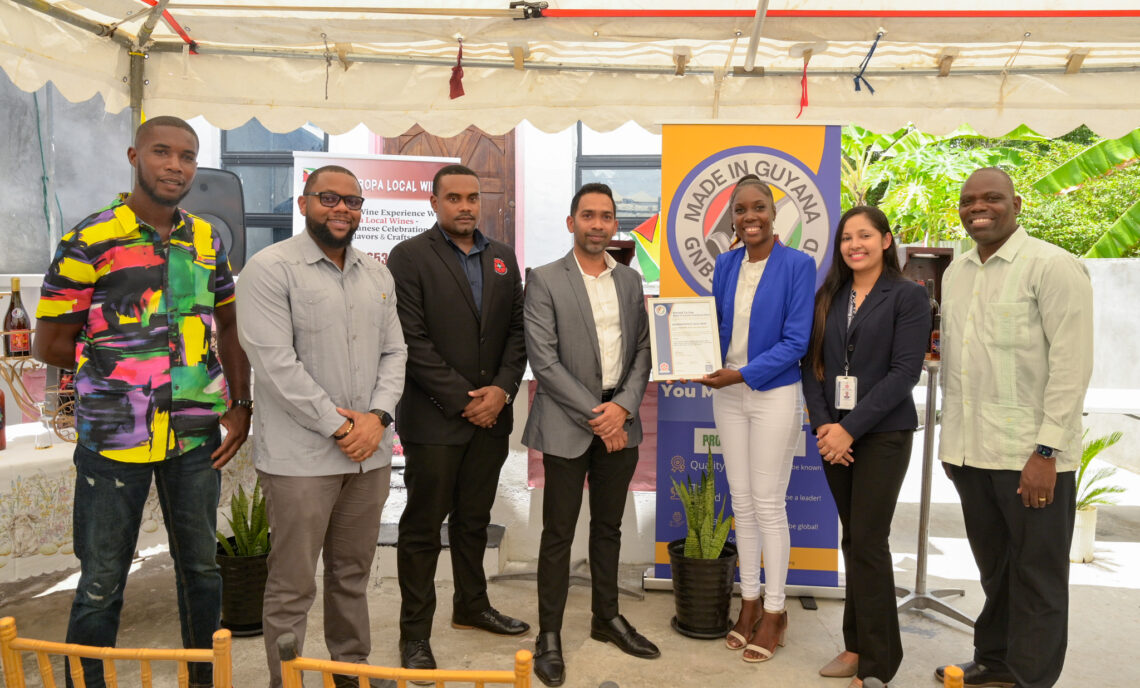 From the right, Communications Officer of MINTIC, Cordell McClure, GNBS Technical Officer, Rosmarie Liliah, Owner of Propa GT Local Wine, Abigale John eagerly displaying GNBS Made in Guyana Certificate, GNBS’ Executive Director, Trevor Bassoo, GNBS Head of Certification Services (Ag.), Keon Rankin and Kevon John.