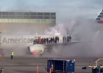Airplane passengers are seen exiting the plane and standing on the wing as smoke rises around them at the Denver airport on Thursday. - @steve_schilsky/X