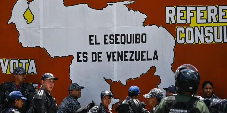 Police and national guard officers next to a mural reading, “Essequibo belongs to Venezuela” during a protest in Caracas this month.Credit...Juan Barreto/Agence France-Presse — Getty Images