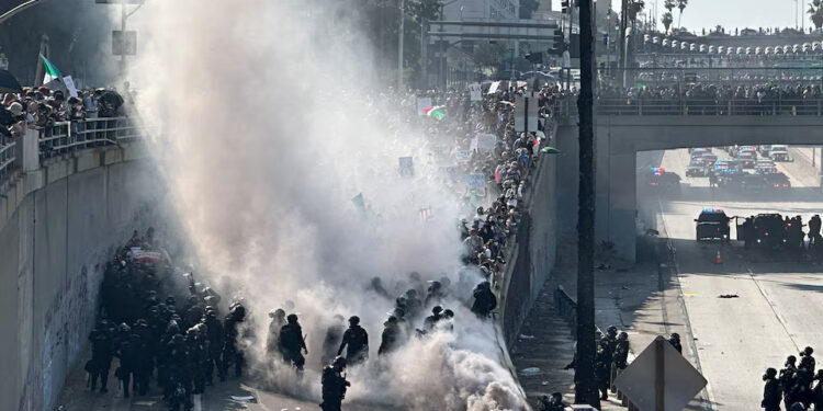 Police officers are enveloped in a cloud of smoke from tear gas and percussion grenades while guarding a highway onramp during a protest against federal immigration sweeps in downtown Los Angeles, California, June 8. REUTERS/Omar Younis