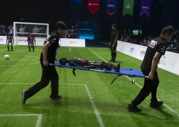 Workers carry out a T1 robot from Booster Robotics during the inaugural RoBoLeague robot soccer competition held in Beijing, Saturday, June 28, 2025. (AP Photo/Ng Han Guan)