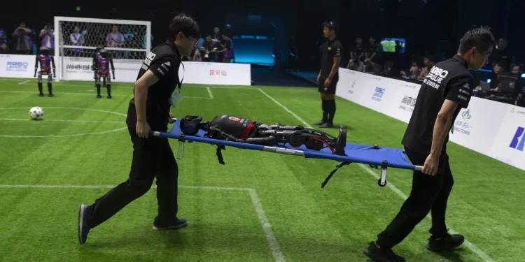 Workers carry out a T1 robot from Booster Robotics during the inaugural RoBoLeague robot soccer competition held in Beijing, Saturday, June 28, 2025. (AP Photo/Ng Han Guan)