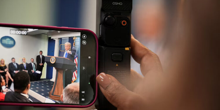 A member of the media records U.S. President Donald Trump speaking during a press conference, after the U.S. Supreme Court dealt a blow to the power of federal judges by restricting their ability to grant broad legal relief in cases as the justices acted in a legal fight over President Donald Trump's bid to limit birthright citizenship, in the Press Briefing Room at the White House in Washington D.C., June 27, 2025. REUTERS/Ken Cedeno/File Photo