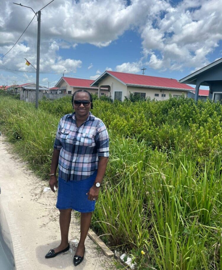 Former APNU+AFC Minister Annette Ferguson standing infront of Great Diamond ECD housing area, showing unoccupied houses and land overgrown with bushes