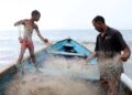 Raesh Ramdass Sr, right, and his son Raesh Jr batch the fish net at Icacos beach on September 3. - Photo by Ayanna Kinsale
