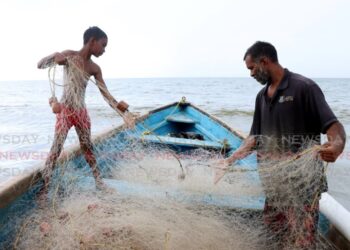 Raesh Ramdass Sr, right, and his son Raesh Jr batch the fish net at Icacos beach on September 3. - Photo by Ayanna Kinsale