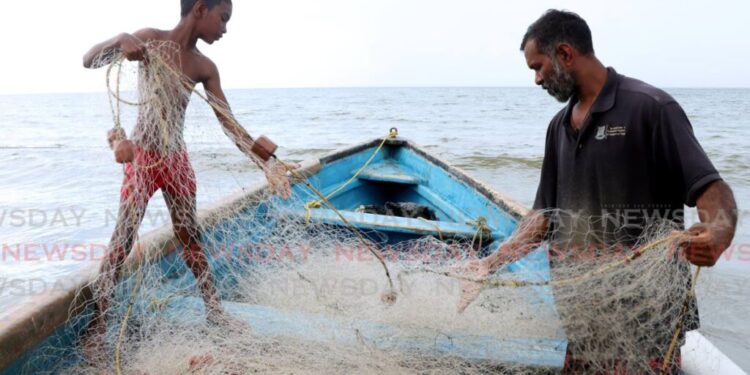Raesh Ramdass Sr, right, and his son Raesh Jr batch the fish net at Icacos beach on September 3. - Photo by Ayanna Kinsale