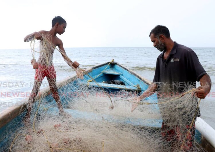 Raesh Ramdass Sr, right, and his son Raesh Jr batch the fish net at Icacos beach on September 3. - Photo by Ayanna Kinsale