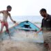 Raesh Ramdass Sr, right, and his son Raesh Jr batch the fish net at Icacos beach on September 3. - Photo by Ayanna Kinsale