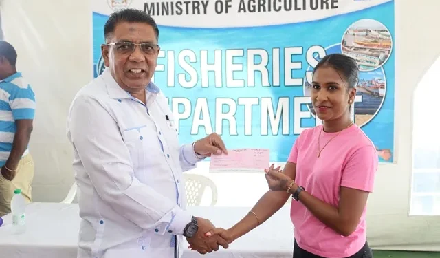 Minister Zulfikar Mustapha handing over a cheque to a female fisherfolk during the distribution at the Everest Cricket Club