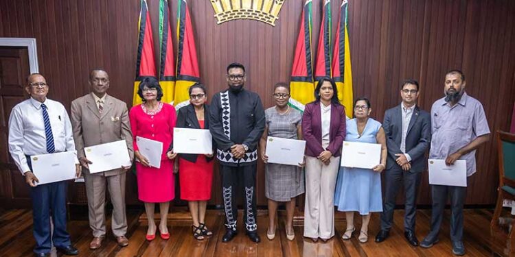 President Dr irfaan Ali (at centre), along with the seven members of the Teaching Service Commission (holding their instruments of appointment) and Minister of Education, Sonia Parag (fourth from right) and Minister of Public Service, Government Efficiency and Implementation (second from right) (Delano Williams photo- Guyana Chronicle)