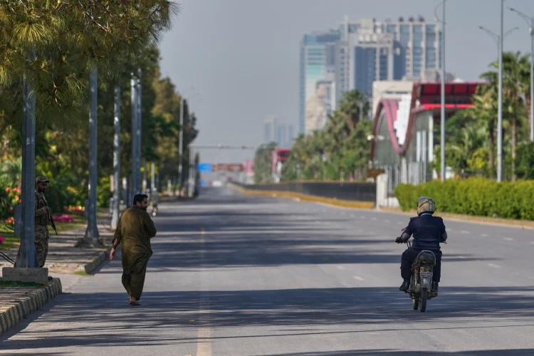 An Army soldier, left, walk as a police officer drives motorcycle on an empty road ahead of  second round of negotiations between U.S. and Iran, in Islamabad, Pakistan Monday April 20, 2026 (AP Photo/ Amjum Naveed)