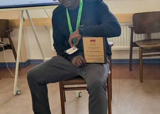 Dr. Lidon Lashley proudly displays his Award for Excellence in Research Review and Analysis at the 2026 International Association for Laboratory Schools (IALS) Conference in Finland.