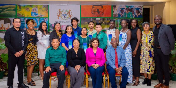 L-R seated: Lecturer of WAP1101 in the Guyanese Languages Unit (GLU), Dr. Adrian Gomes; Vice-Chancellor, Professor Paloma Mohamed Martin; Minister of Local Government and Regional Development, Hon. Priya Manickchand, MP; and Deputy Vice-Chancellor for Academic Engagement, Professor Emanuel Cummings.
R-L standing: Dean of the Faculty of Engineering and Technology, Dr. Kofi Dalrymple; Lecturer in the GLU, Ms. Charlene Wilkinson; Director of the International Centre of Excellence for Modern and Indigenous Languages, Literatures and Linguistics, Dr. Penelope Montfort; 9 students who graduated from the inaugural Wapichan Language Course; Coordinator of the GLU, Dr. Tamirand Nnena De Lisser; and Principal Regional Development Officer, Ministry of Amerindian Affairs, Mr. Anil Roberts.