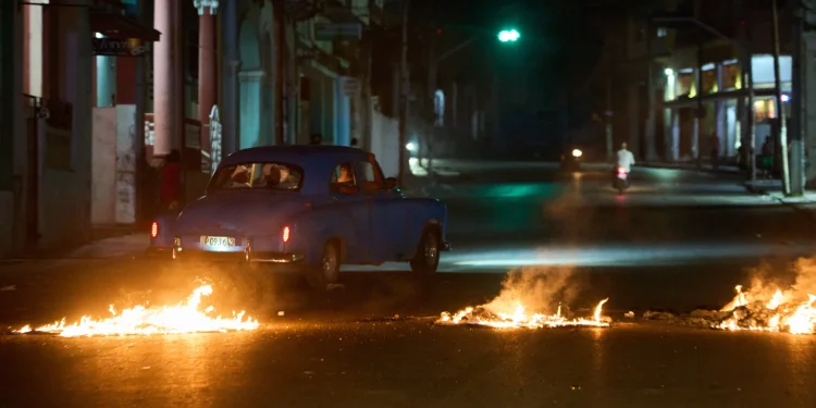 People drive a classic American car through a barricade set up by residents protesting against prolonged power outages in Havana, Cuba, Wednesday, May 13, 2026. (AP Photo/Ramon Espinosa)