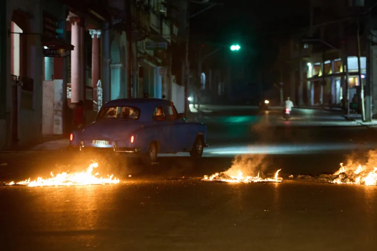People drive a classic American car through a barricade set up by residents protesting against prolonged power outages in Havana, Cuba, Wednesday, May 13, 2026. (AP Photo/Ramon Espinosa)