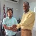 CEO of Nations University, Dr. Dexter Phillips, presents Emmanuel Pereira with the contribution from School of the Nations