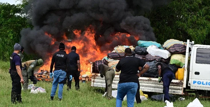 beating the heat: Commissioner of Police Allister Guevarro, centre, quenches his thirst as he oversees the destruction of large quantities of illegal drugs during a TTPS exercise yesterday at the Caroni Cremation Site. —Photo: JERMAINE CRUICKSHANK