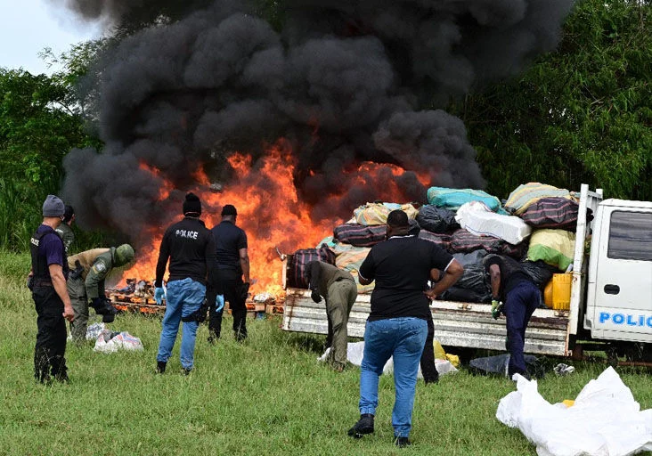 beating the heat: Commissioner of Police Allister Guevarro, centre, quenches his thirst as he oversees the destruction of large quantities of illegal drugs during a TTPS exercise yesterday at the Caroni Cremation Site. —Photo: JERMAINE CRUICKSHANK