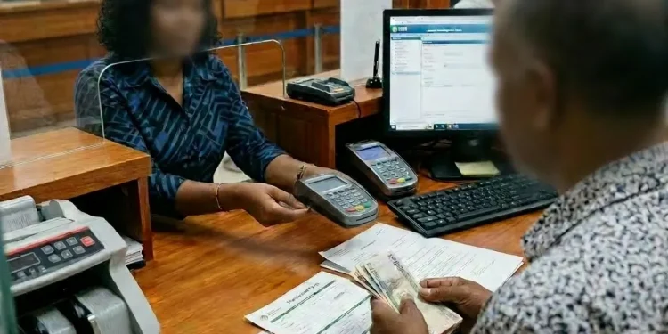 A bank teller assisting a customer with currency and documents at Guyana Development Bank