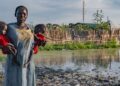 © UNICEF A woman holds her children in front of her flood-affected house in South Sudan.