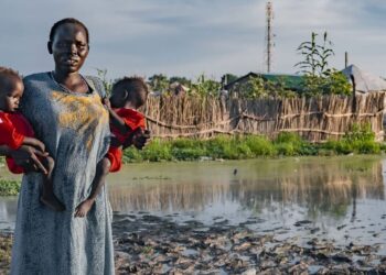 © UNICEF A woman holds her children in front of her flood-affected house in South Sudan.