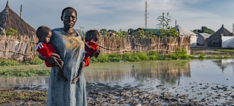 © UNICEF A woman holds her children in front of her flood-affected house in South Sudan.