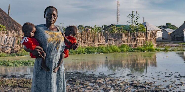 © UNICEF A woman holds her children in front of her flood-affected house in South Sudan.