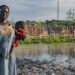 © UNICEF A woman holds her children in front of her flood-affected house in South Sudan.
